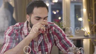 穿着衣服的中东男人在咖啡馆里喝着热茶，看着远处，摇头，<strong>签约</strong>。 令人担忧的年轻画像